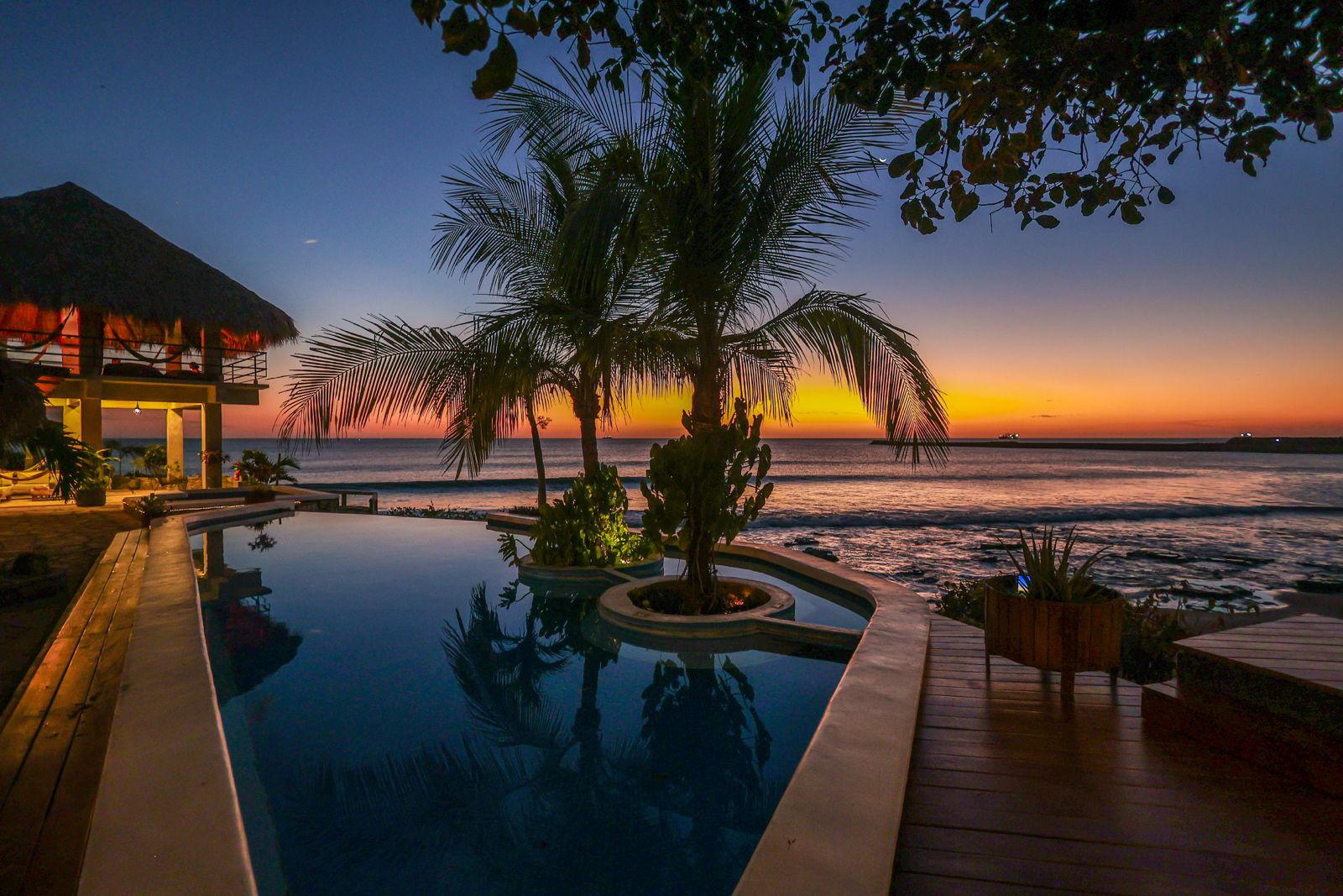Infinity pool and deck at Miramar Surf Camp at dusk, with palm trees and the ocean behind